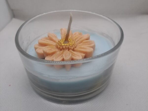 Add a touch of elegance and serenity to your home with this beautifully handcrafted floral candle. Featuring a delicate peach flower with a shimmering golden center, set on a soft sky-blue wax base inside a premium clear glass jar, this candle is perfect for creating a warm and relaxing atmosphere.